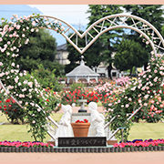 愛をつなぐアーチの写真 薔薇に囲まれたハート形のアーチの足元にかわいらしい男女の像がある