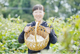 作物を入れたかごをこちらに見せ微笑んでいる女性の写真