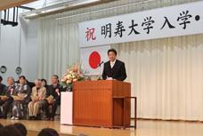 平成30年度明寿大学入学式及び進級式で、壇上でお話しされる市長の写真です。左奥には来賓席があり、8名ほどの来賓が座っています。