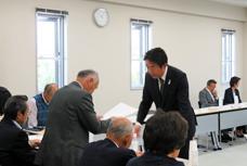 第20回富士見地区地域審議会の写真です。白い壁の会議室の中にコの字形に机がレイアウトされています。出席者のうちの一名と市長が書類のやりとりをしています。