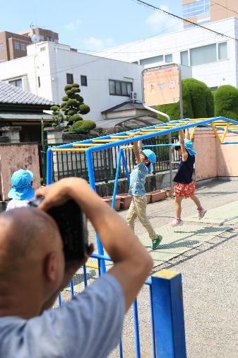 保育所の遊具で遊ぶ子供たちの写真を撮るカメラマン