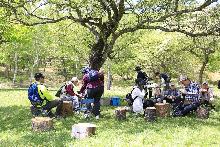 木陰の下に座ってお茶を飲んだりして一休みするハイキングツアーの参加者たち