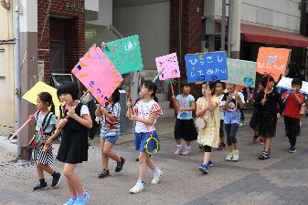 願いを書いたプラカードを掲げてまちなかを行進する子どもたち