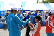 走り終えた子どもに参加賞の飲み物を渡す中学生ボランティアの写真