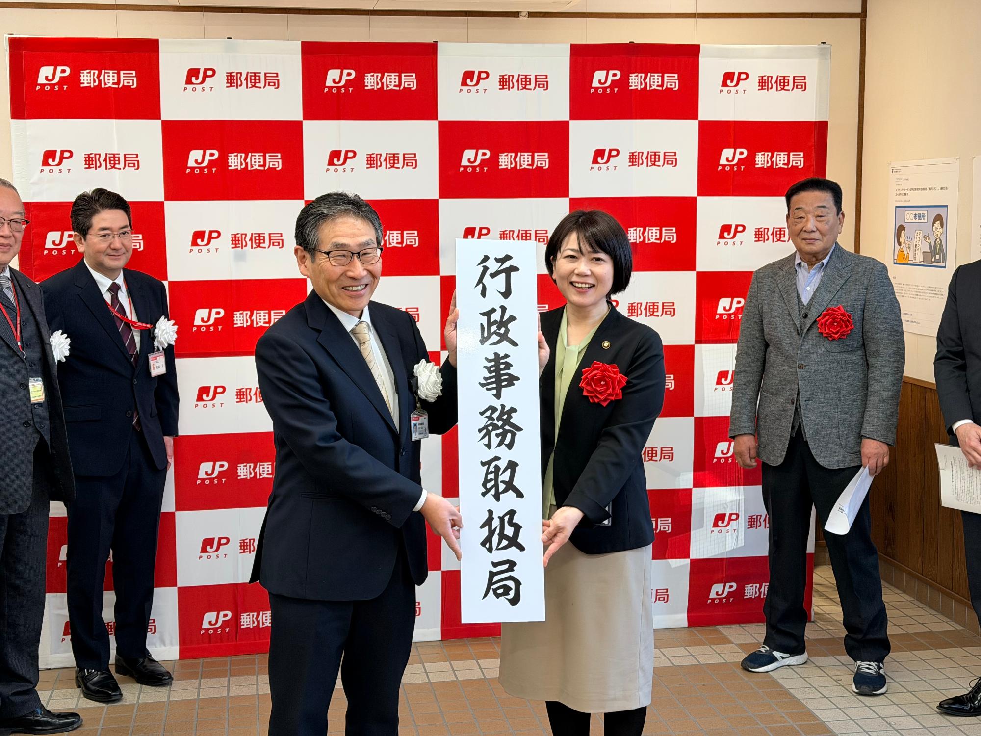 行政事務取扱局という看板を手にする小川市長と郵便局関係者