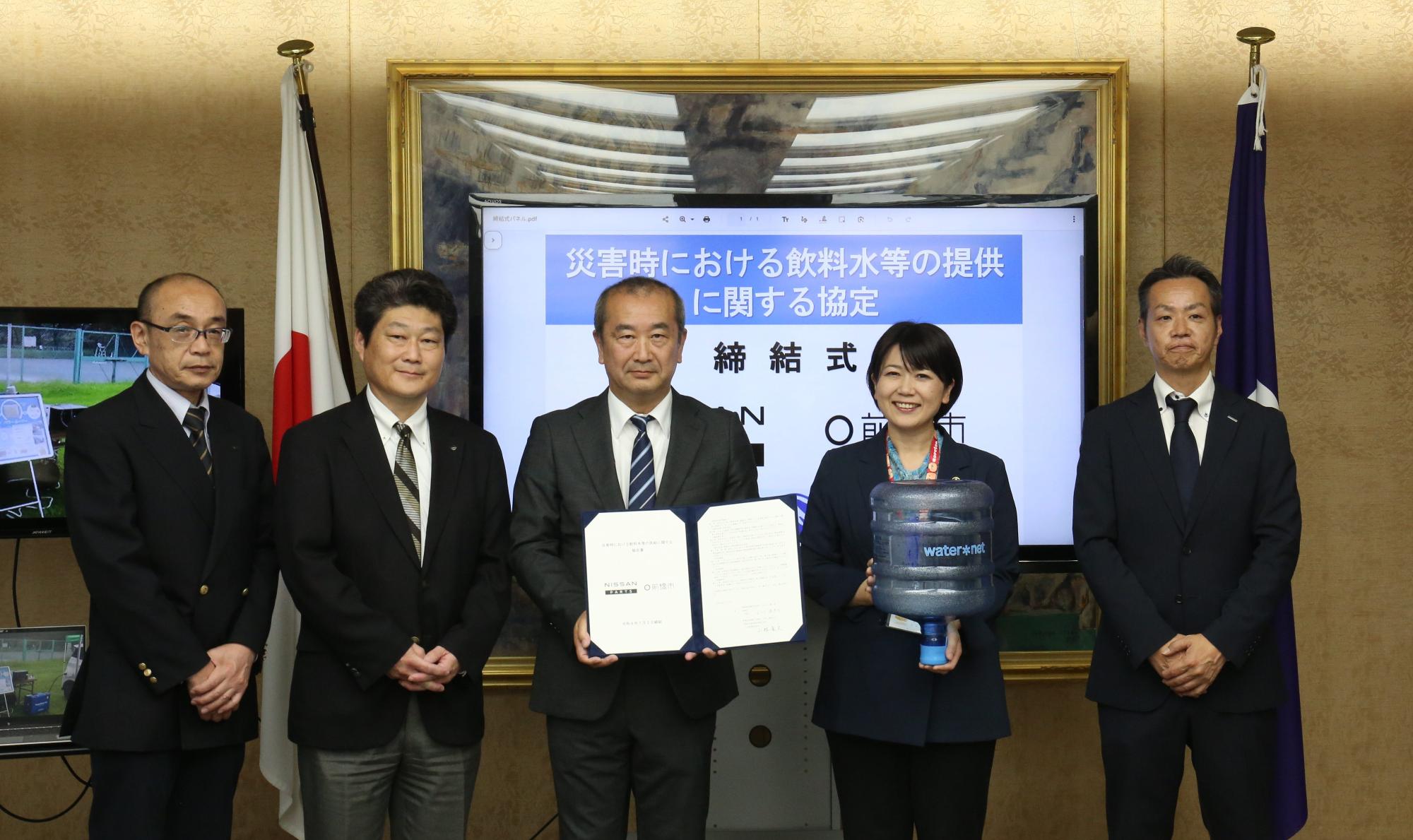 協定書や水タンクを持って記念撮影する関係者と小川市長