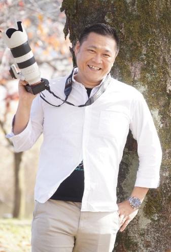 佐藤さんが木の前で笑顔の写真