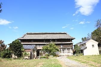 青空の下にそびえ立つ大きな塩原家住宅の外観写真