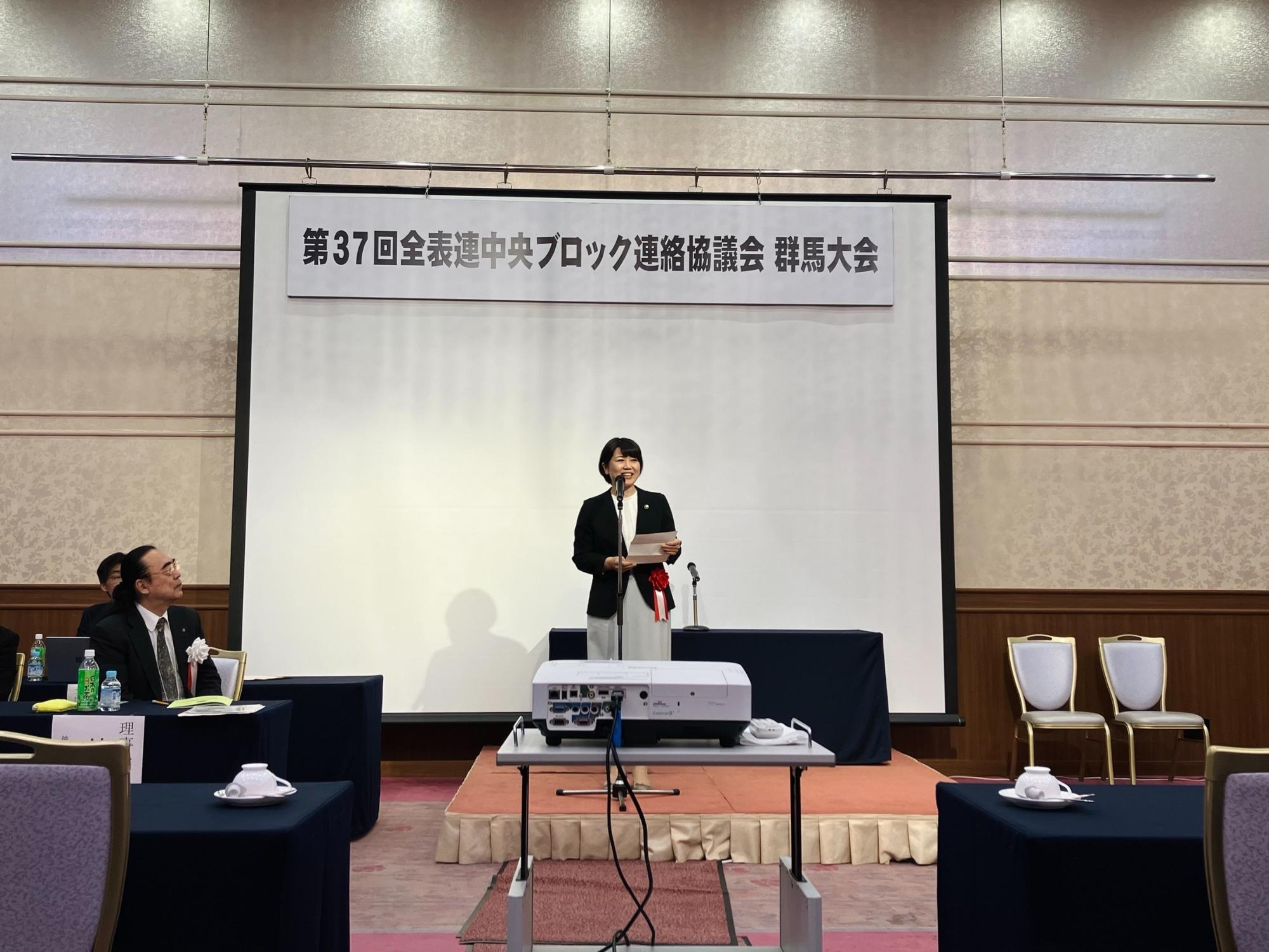 スクリーンの前であいさつをする小川市長