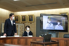 オンライン開講式のために設置されたモニター越しに挨拶する山本市長の写真