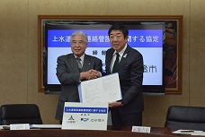 吉岡町との上水道相互連絡管設置に関する協定締結のため、吉岡町長と協定書を交わして握手している市長の写真です。