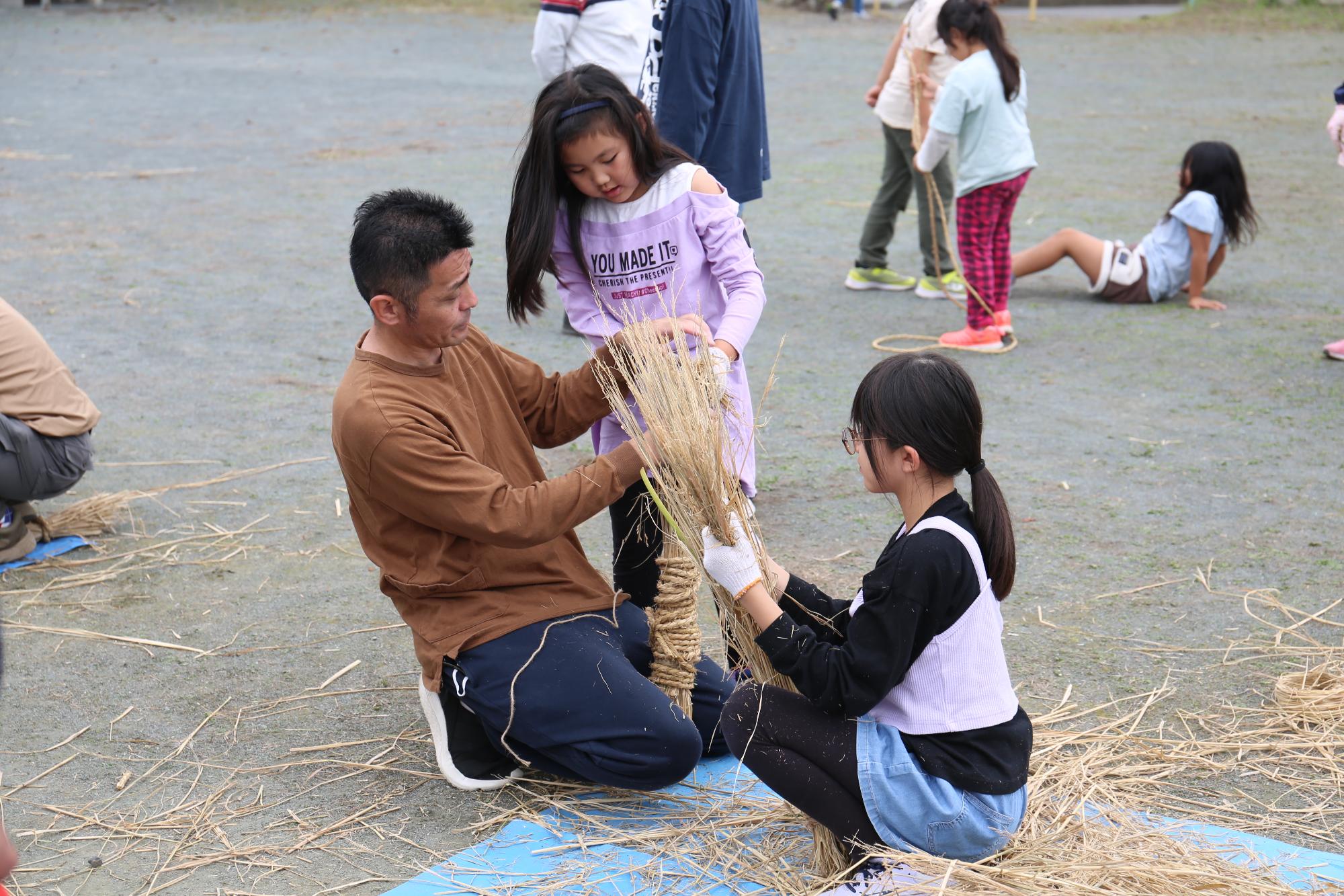 わら鉄砲をつくる大人と子ども