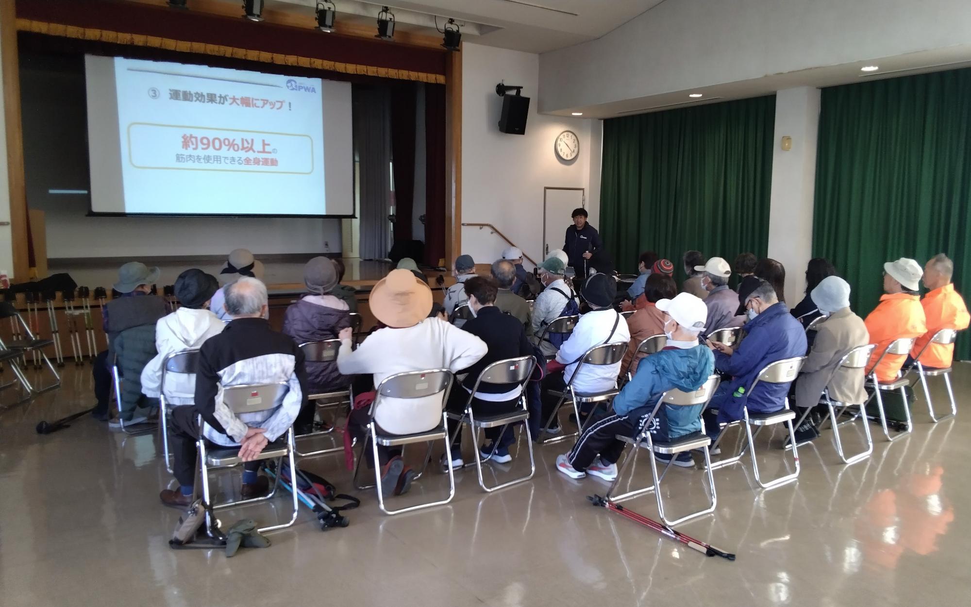 講師からポールウォーキングの効果を聞く参加者