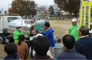 自主防災会防災訓練で給水タンク車の説明を受ける参加者の写真