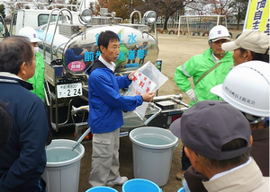 自主防災会防災訓練で非常用飲料水袋の説明を受ける参加者の写真